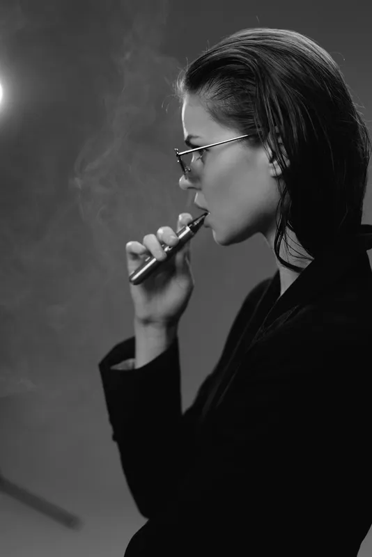 Woman vaping with glasses in black and white, profile view with smoke, stylish and modern concept.
