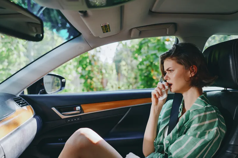 A woman sits in the driver's seat of a car, resting her hand near her lips, thoughtful and calm.