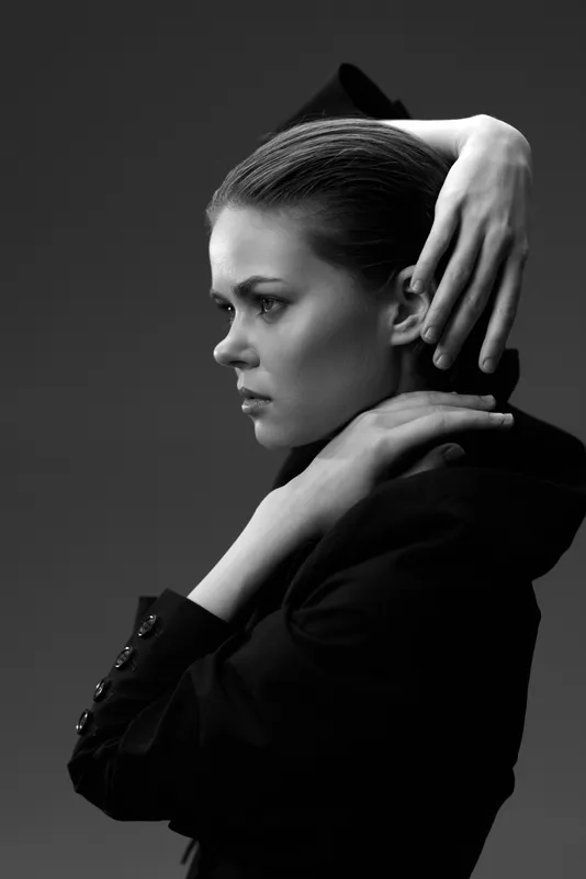 Black and white portrait of a serious woman in a suit with slicked-back hair, showing elegance and confidence in a studio setting.
