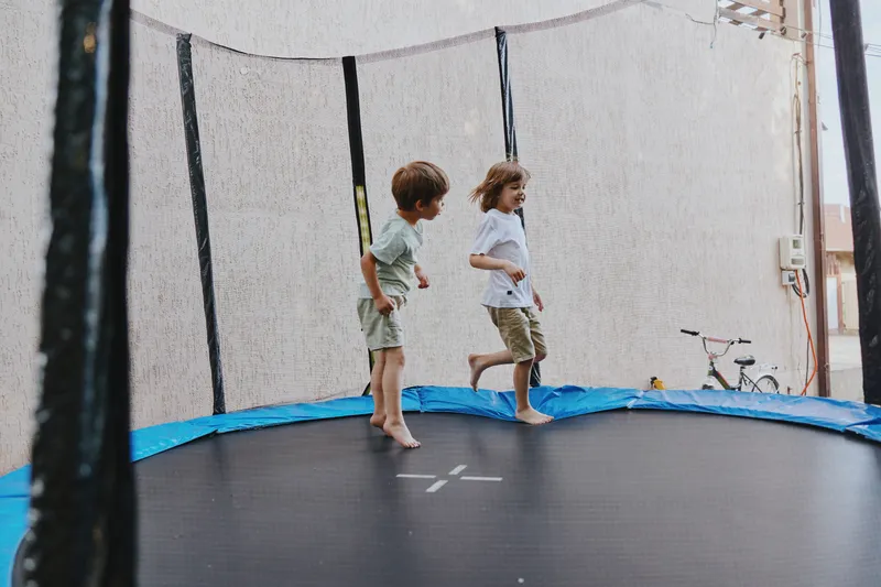 Happy children jumping on a trampoline, enjoying their time outdoors with bright smiles and energetic movements. Perfect for expressing joy and childhood fun. ###