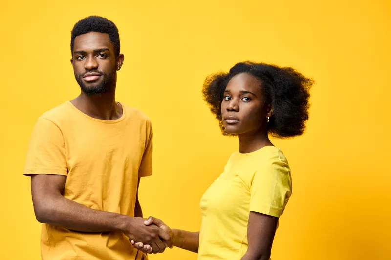 Young African couple shaking hands against a vibrant yellow background, showcasing partnership and trust, dressed in matching yellow outfits, expressions of determination