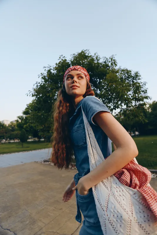 lifestyle woman in modern boho-western denim street style with long hair and red bandana enjoying outdoors in natural park setting, film color tones