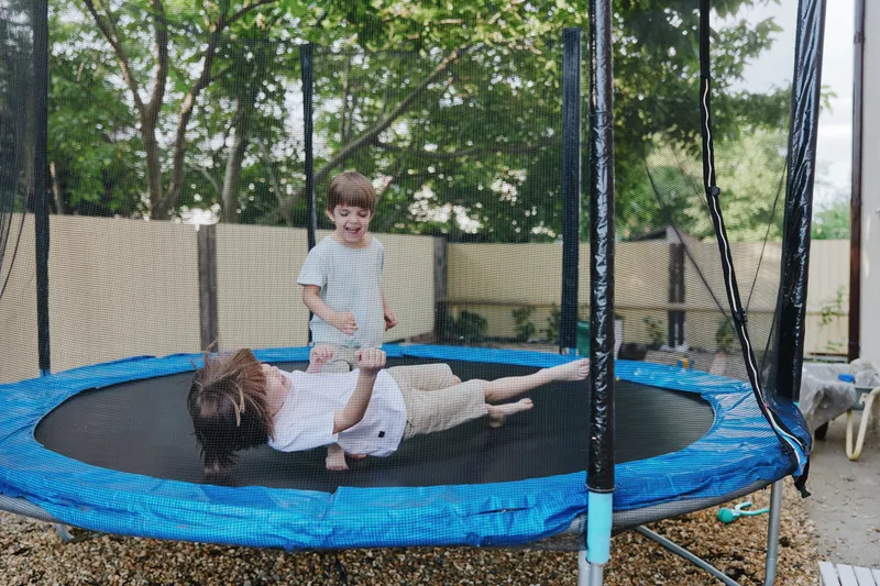 Happy children playing on a trampoline, enjoying a sunny day with laughter and excitement in a vibrant garden setting.