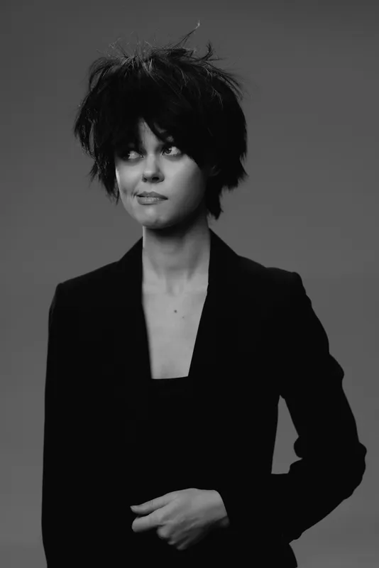Black and white portrait of a stylish woman with short messy hair wearing a black blazer and looking sideways.