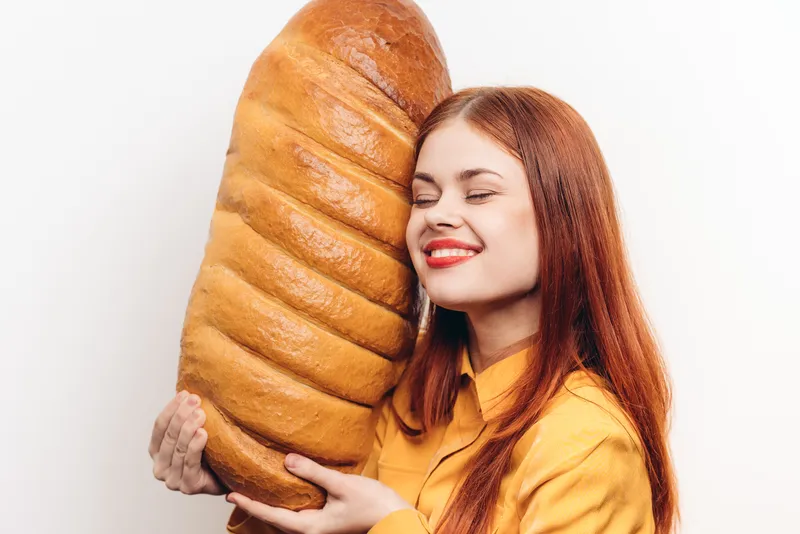 Счастливая женщина обнимает буханку хлеба, мучной продукт, светлый фон, обрезанный вид