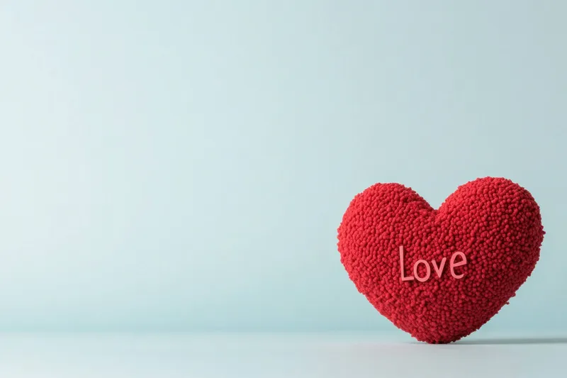 Яркий красный объект в форме сердца с надписью «Love» на мягком пастельно-голубом фоне