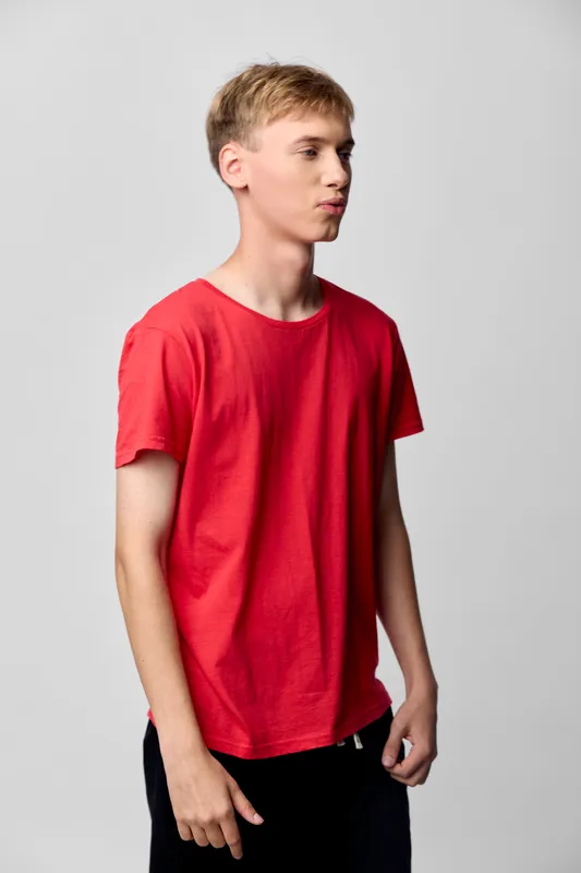 Young man in a red tshirt poses in a clean studio, lips puckered, casual fashion vibe with bold color focus, simple background, relaxed stance, modern style for fashion or lifestyle shoot