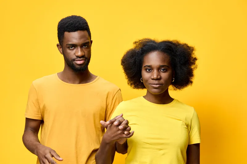 Young African couple holding hands, wearing yellow t shirts, smiling with vibrant energy against a bright yellow background, symbolizing love and connection