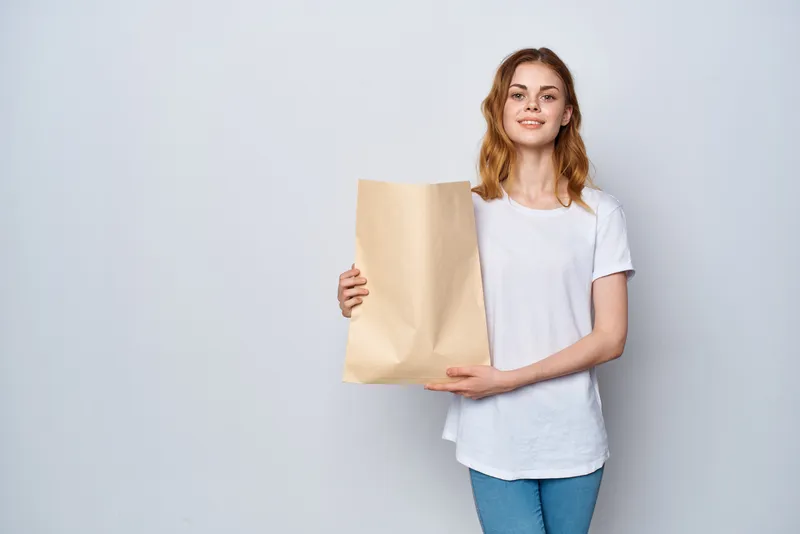 Женщина в белой футболке держит пакет с продуктами, совершая покупки