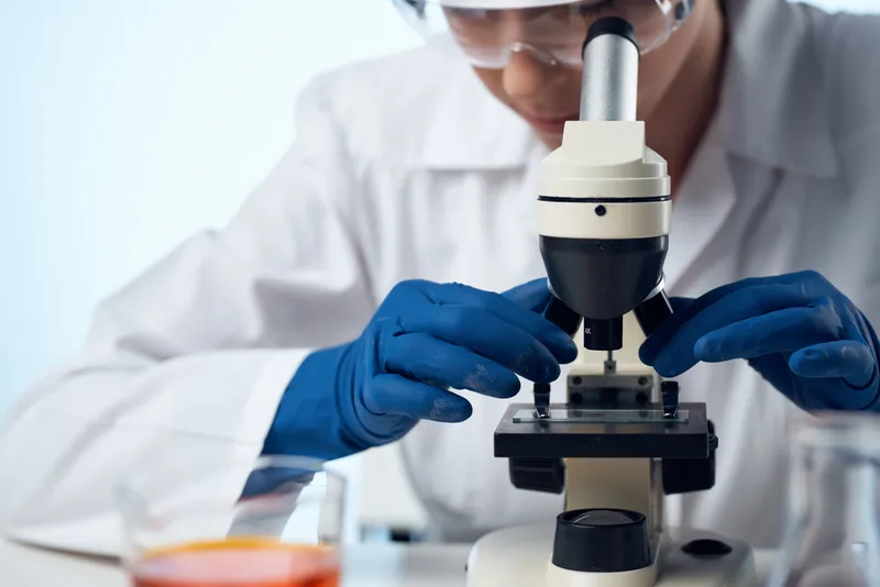 Женщина-лаборант работает за столом с микроскопом, профессионально выполняя свои обязанности