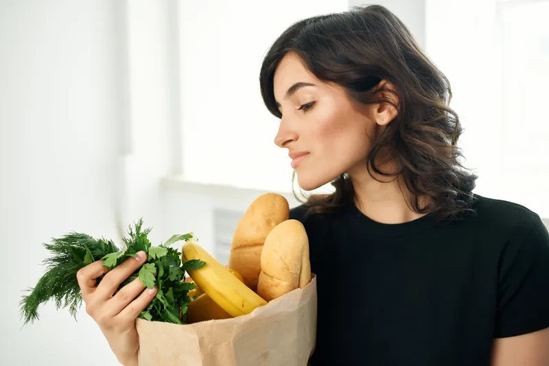 Женщина с пакетом продуктов для здорового питания занимается приготовлением еды и покупками
