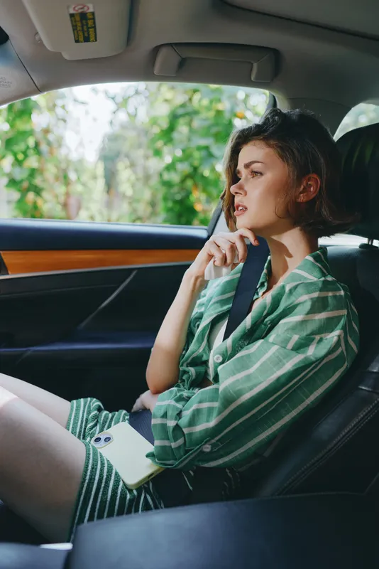 A woman sits in a car interior with a seatbelt fastened, her thoughtful gaze toward the window, illuminated by soft natural light.