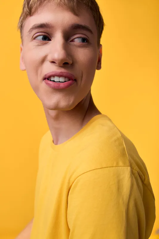 Young man in a yellow shirt against a bright yellow backdrop, casual pose, candid expression conveying warmth, confidence and creative energy in studio photography