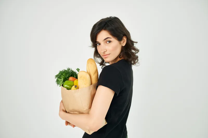 Симпатичная женщина с пакетом продуктов, здоровое питание, овощи, светлый фон