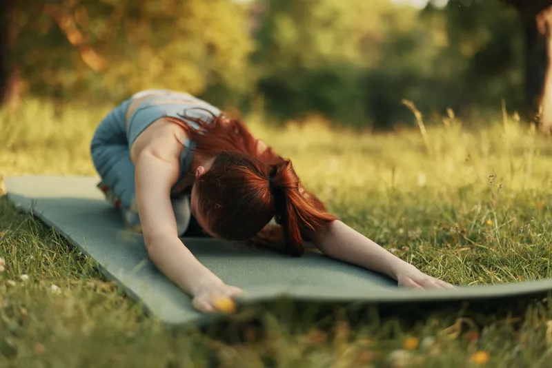 A woman practicing yoga in a serene outdoor setting during a sunny day, embodying tranquility and mindfulness while stretching on a yoga mat