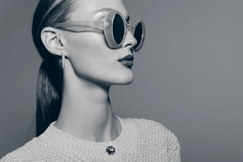 Portrait of elegant caucasian woman with pale skin wearing round sunglasses and textured sweater looking sideways. Concept of fashion, style, beauty, and confident female model in monochrome.