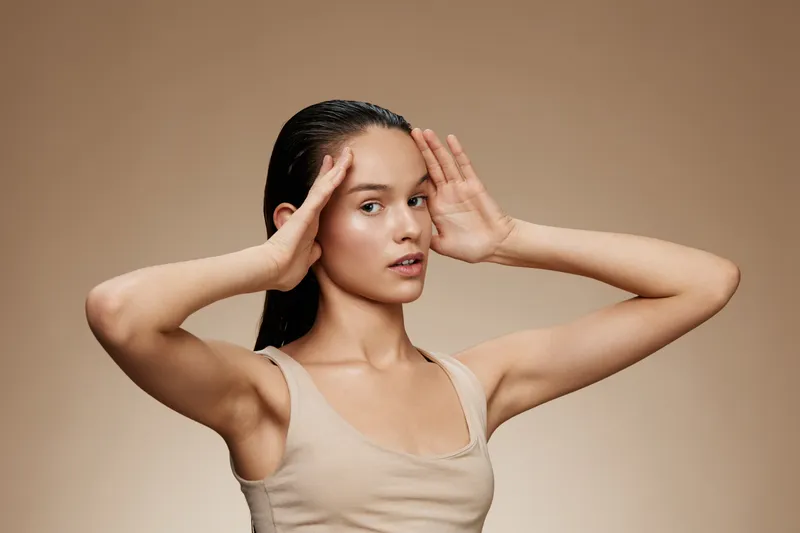 Young female model with long hair striking a serene pose against a warm brown background, conveying calmness and mindfulness, ideal for wellness concepts