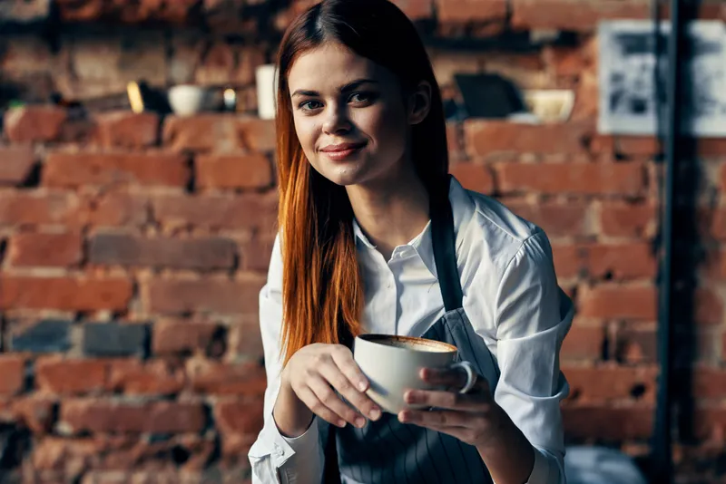 Женщина с чашкой кофе стоит возле столика