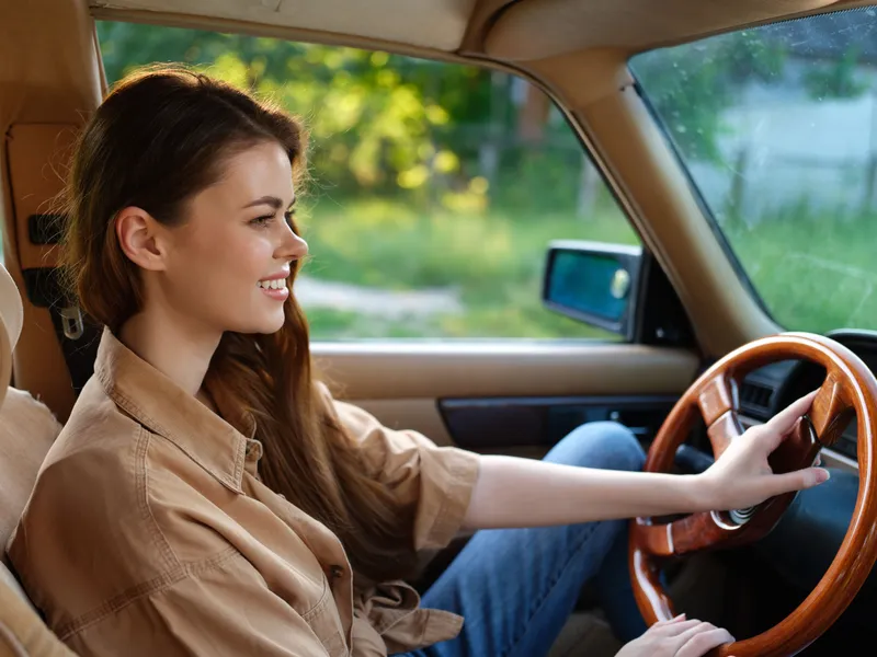 Smiling young woman driving a vintage car, wearing casual clothing, with a vibrant green background, evoking a sense of freedom and adventure.