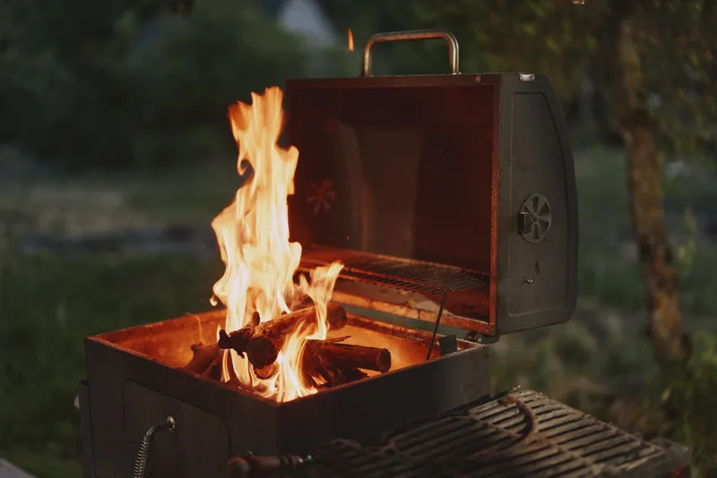 Cozy outdoor barbecue with flames, showcasing a grill filled with burning wood, creating a warm atmosphere, ideal for summer gatherings and family dinners