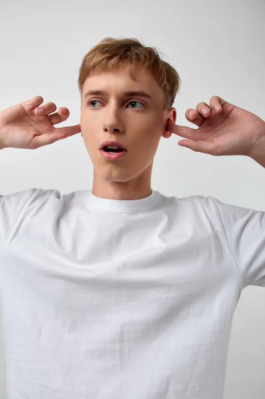 Surprised expression on a casual man in a white shirt, hands near ears, capturing curiosity and attentive listening, emotion of astonishment suitable for lifestyle, reaction, or awareness themes