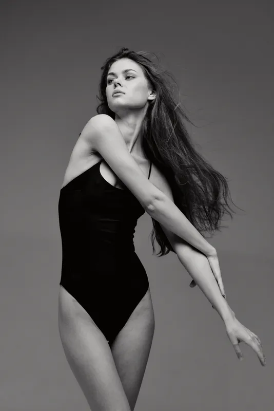 Elegant black and white portrait of a young woman in a black bodysuit with flowing hair and graceful pose