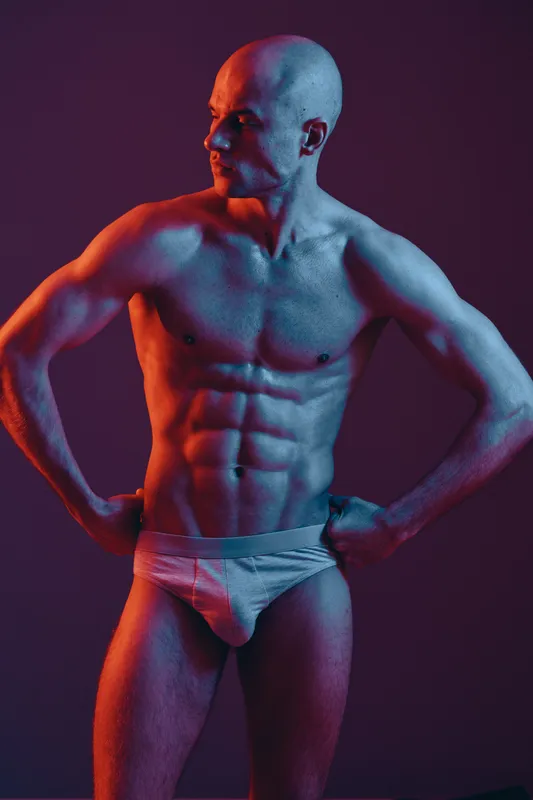 Strong man showcasing muscular physique under vibrant lighting, emphasizing shapes and shadows, creating an engaging visual effect.