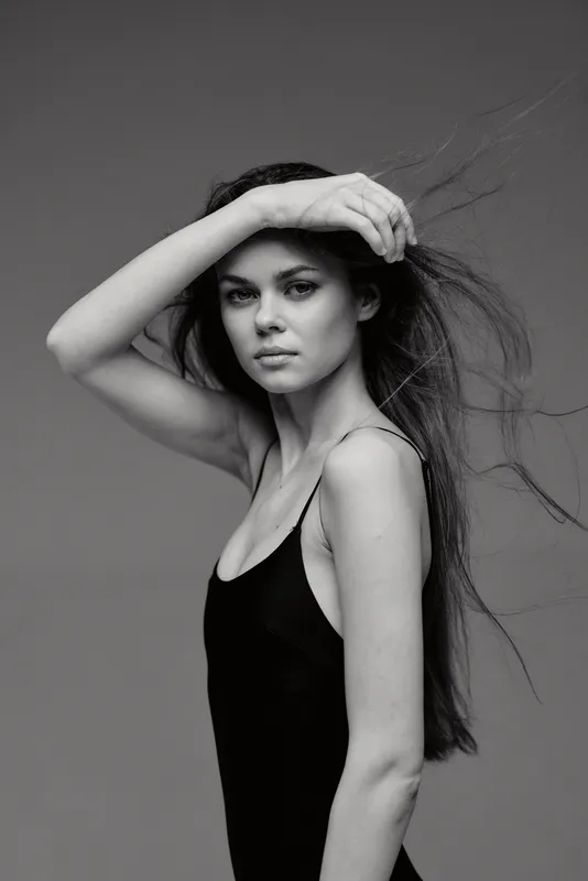 black and white portrait of a serious woman with long hair in a simple black dress and natural makeup