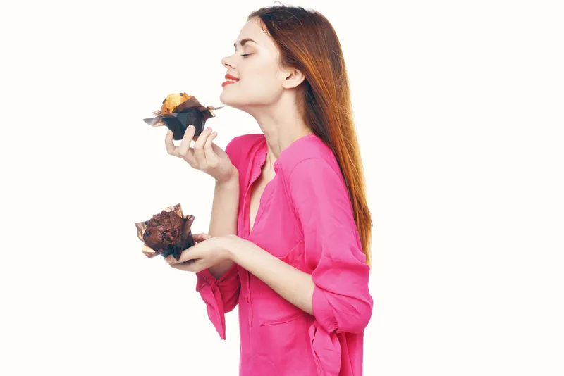 Миловидная женщина держит в руках капкейк и перекусывает сладостями