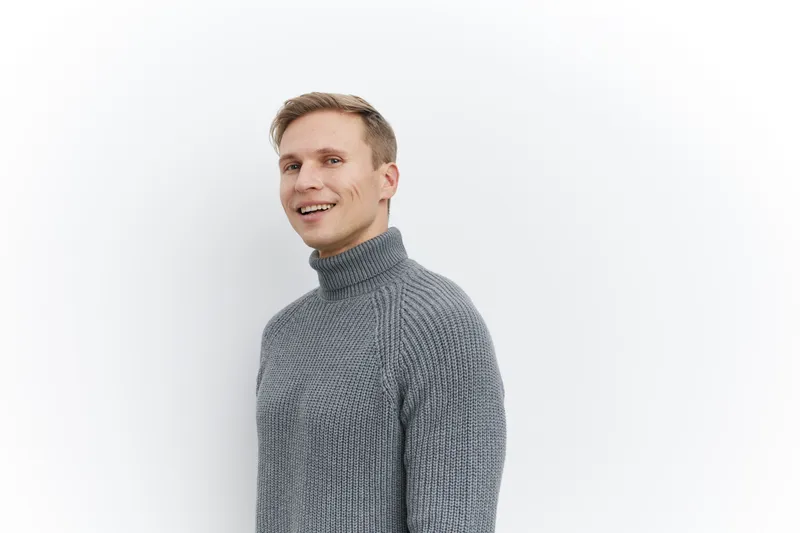 Smiling man wearing gray turtleneck sweater looking at camera isolated on white background studio portrait. People lifestyle concept, casual, cheerful, happy, facial expression, fashion.