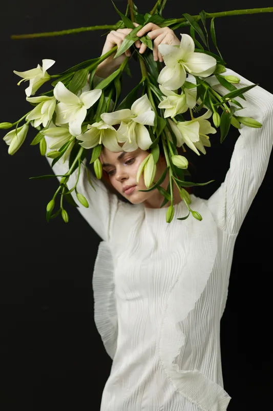 Woman wearing an elegant white dress adorned with flowers, conveying tranquility and beauty in a dark background for a fashion or nature themed project