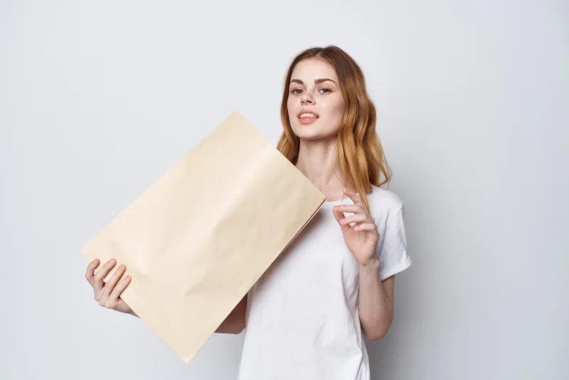 Привлекательная женщина в белой футболке держит в руках пакет с покупками