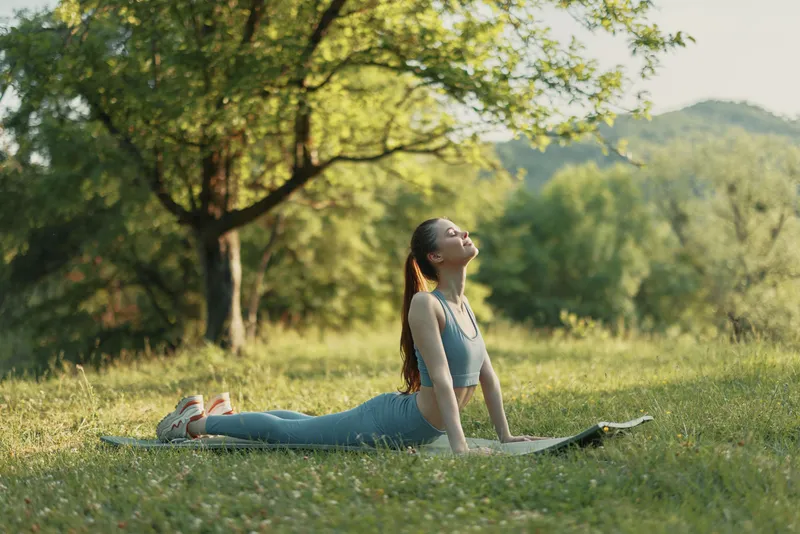Young woman practicing yoga in nature during a sunny day, wearing workout attire, radiating calmness and focus, surrounded by greenery, promoting wellness and mindfulness
