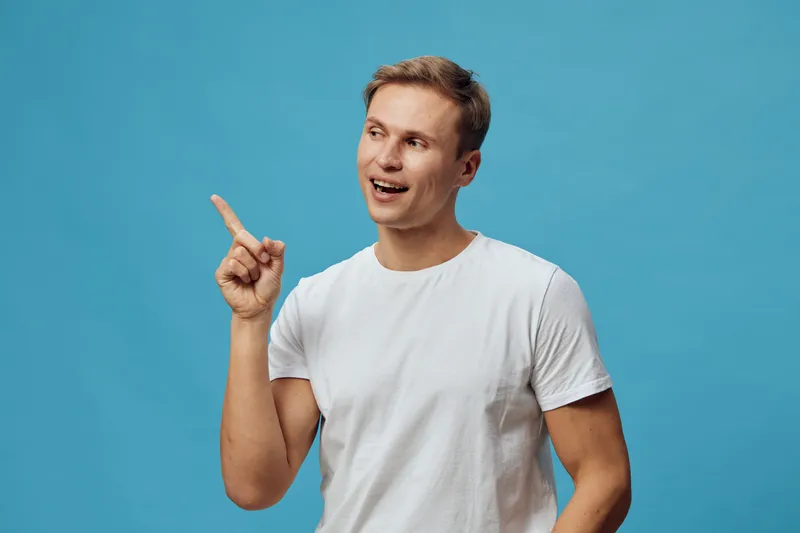 smiling young man finger point looking sidewear white tshirt isolated blue background digital nomad freelance work concept