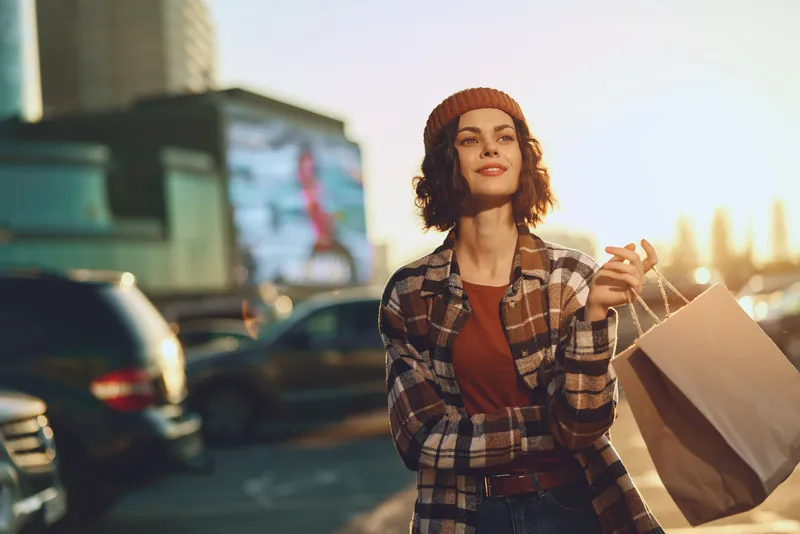 Woman shopping in urban street portrait at sunset, candid smile and bag in hand, golden hour glow and authenticity evoke mindful living and emotional storytelling in modern city lifestyle