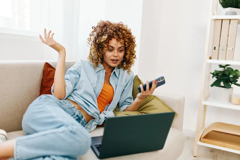 Улыбающаяся женщина использует ноутбук для онлайн-работы фрилансера в уютной и современной гостиной