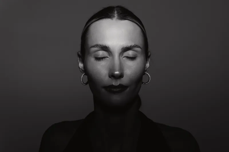 Young Caucasian woman with fair skin and closed eyes illuminated by dramatic lighting on a dark background. Concept of calm, serenity, and introspection.