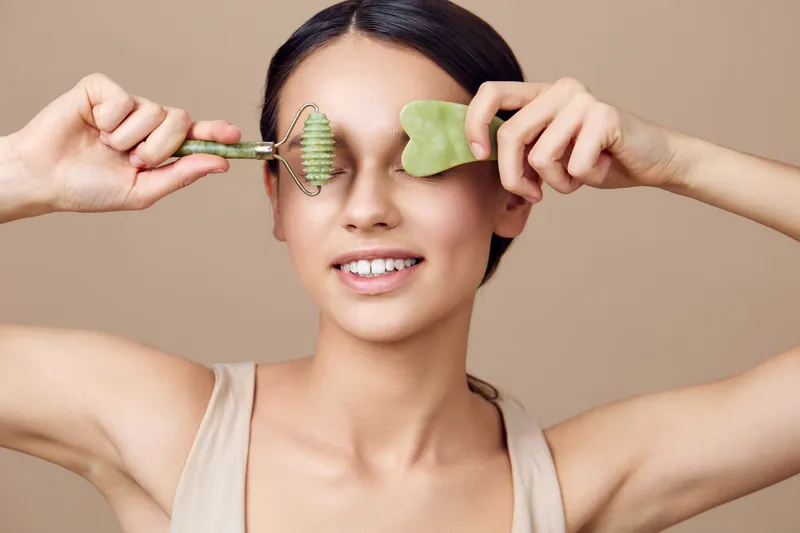 A young woman using jade rollers for facial massage, showcasing natural beauty, relaxation, and skincare in a minimalist setting