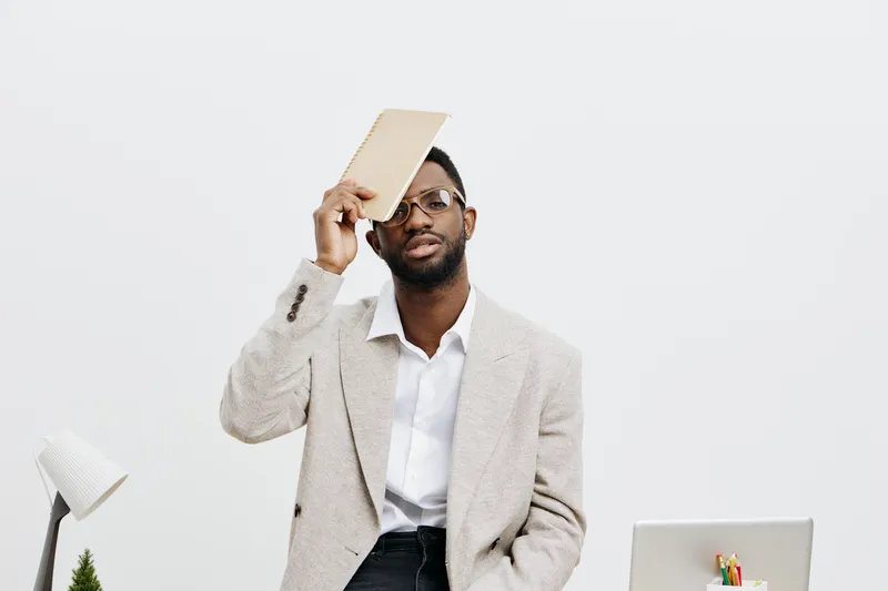 Professional man in business attire holding a clipboard near face, looking serious, in an office environment with a white background. Modern workplace concept for leadership, management, and professio