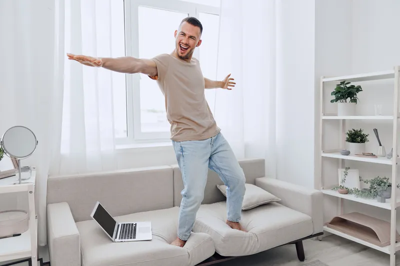 Energetic man enjoying life while balancing work and personal time, celebrating emotional minimalism and authentic imperfection in a cozy home setting.