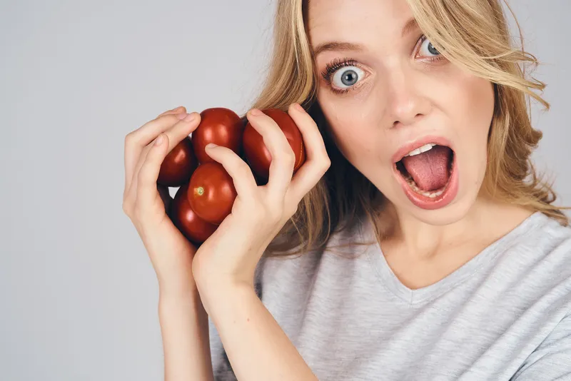 Эмоциональная женщина с продуктами в руках на сером фоне, еда, модель, обрезанный вид