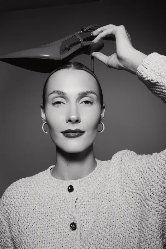Elegant white woman with fair skin holds high heel shoe above head in black and white portrait. Concept of fashion, style, and creativity.