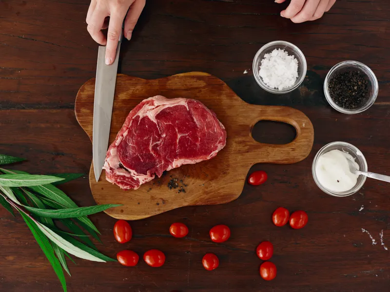 Женщина с ножом в руке нарезает свежее мясо стейка для жарки на кухне