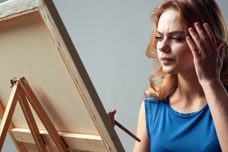 Женщина-художница с кистью и красками у мольберта, искусство, хобби, светлый фон