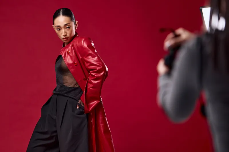 Азиатская модная фотосессия с женщиной в красном кожаном пальто и брюках, позирующей на красном фоне, в то время как фотограф снимает ее