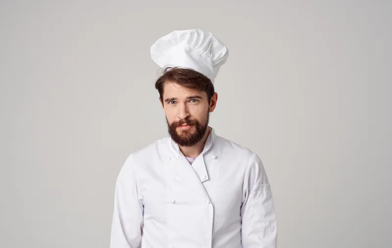Бородатый шеф-повар профессионально работает на кухне, на сером фоне