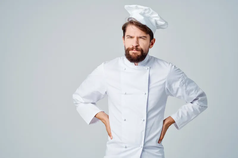 Бородатый мужчина в рабочей униформе, его профессия связана с кухней, на светлом фоне