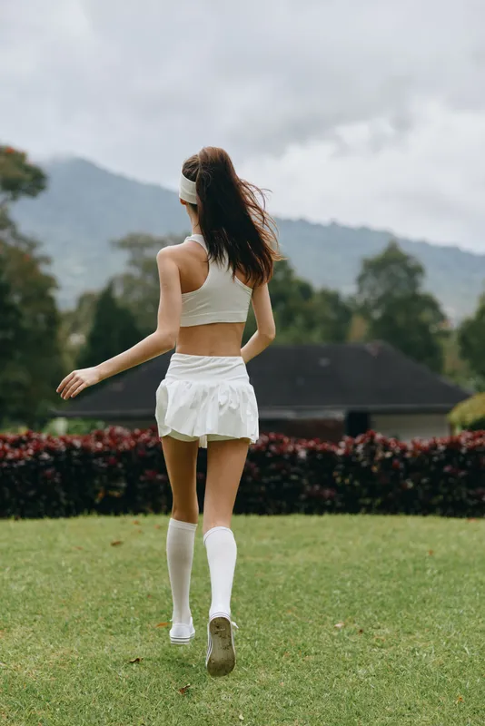 Sportswoman jogging in white athletic clothing, showing determination and fitness against a vibrant nature background, embodying health and vitality