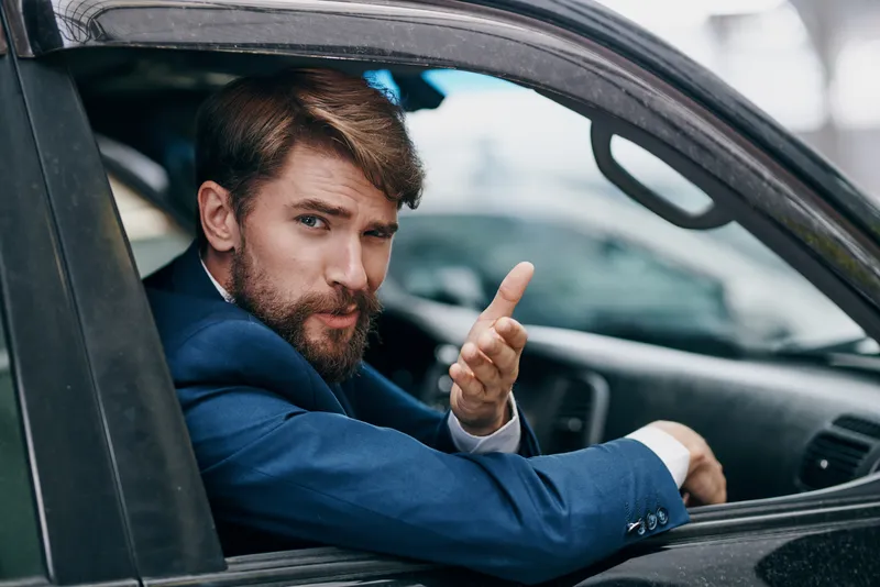 Мужчина в деловом костюме выглядывает из окна автомобиля
