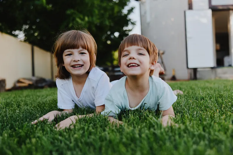 Joyful children laughing on green grass, enjoying a sunny day outdoors, showcasing the innocence and happiness of childhood in a warm and vibrant atmosphere.